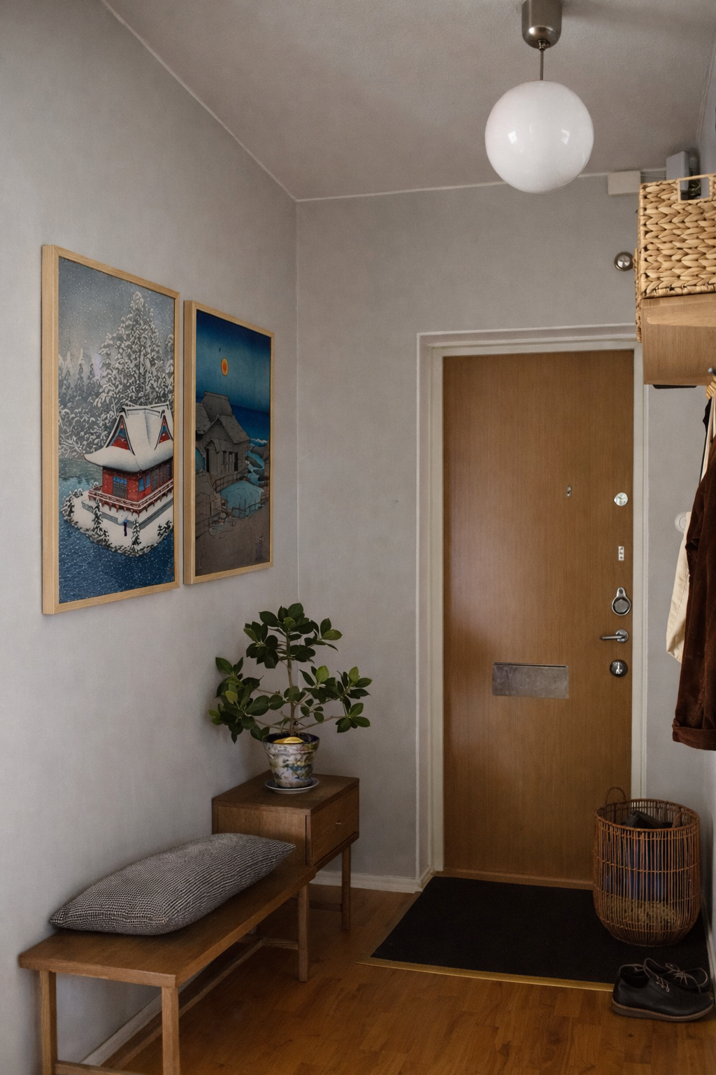 Narrow hallway with wooden bench, plant, and framed pictures on a light gray wall.