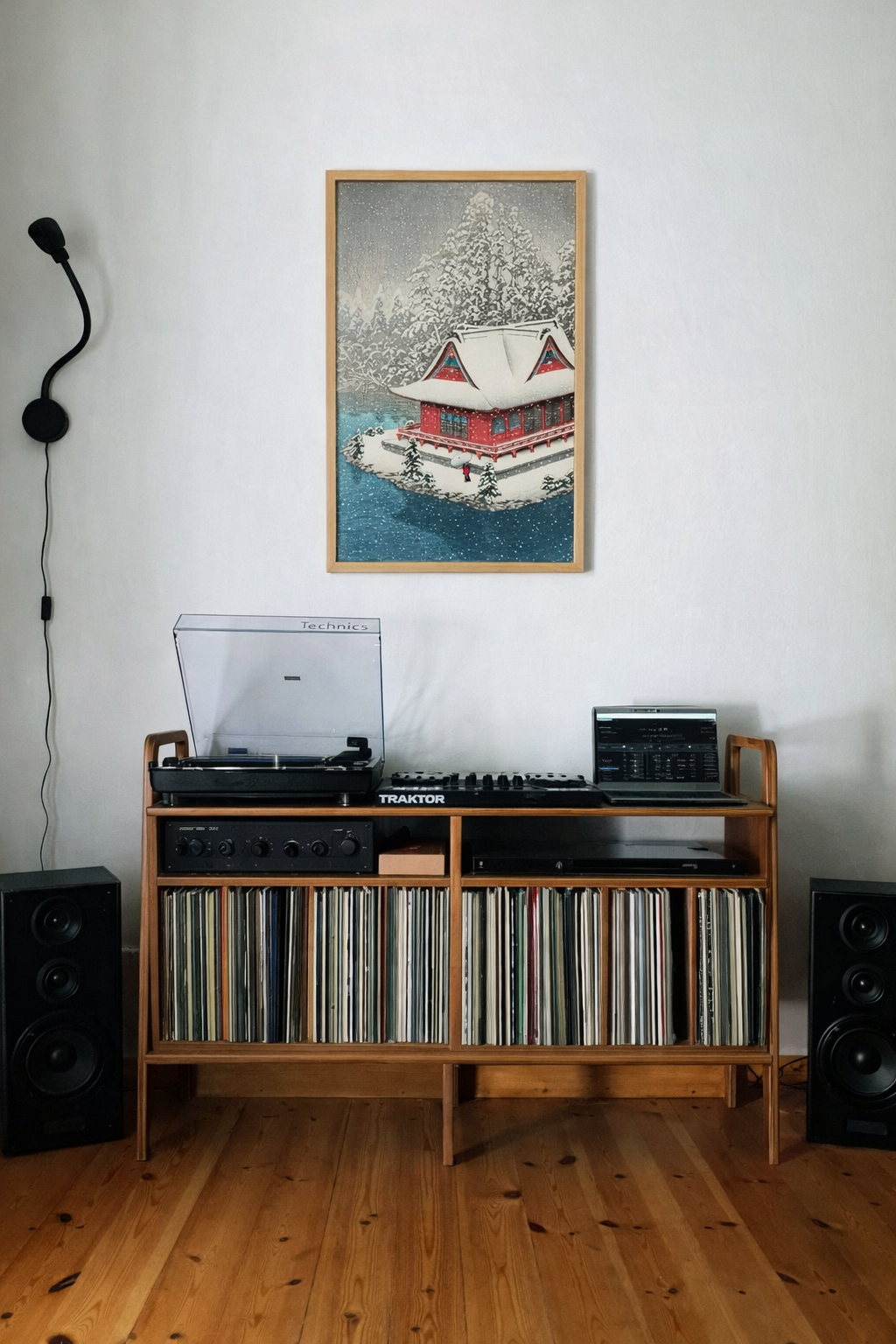 Wooden record player console with vinyl records, speakers, and a framed picture on a white wall.