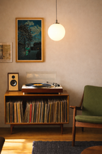 Record player with vinyl records on a wooden cabinet in a room with a green sofa and framed picture on the wall.